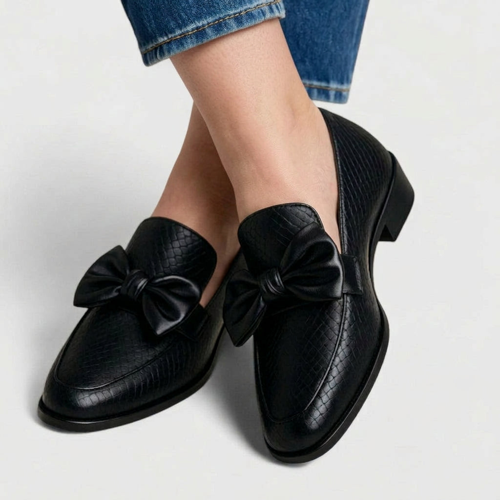 Black textured bow-detail loafers worn with cropped jeans, angled top view