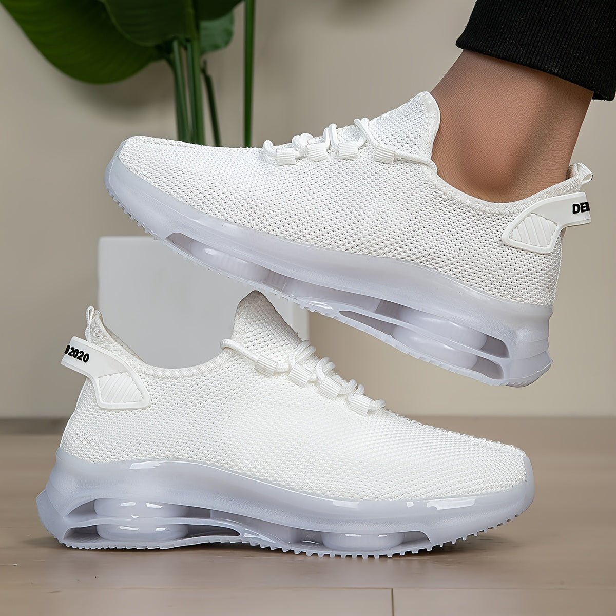 White knit trainers, side view, one worn on foot and one placed on the floor